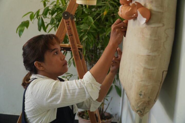 Nurul Inayah sedang menempelkan cangkang telur di atas kasur yang dijadikan kanvas (Aku Ingin Tidur Lelap)