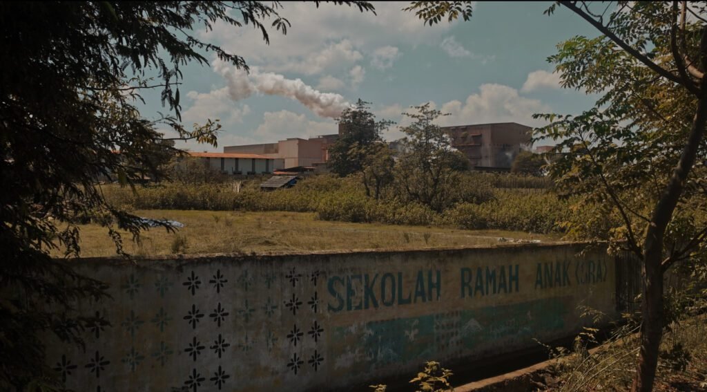 Tulisan ‘SEKOLAH RAMAH ANAK’ di salah satu sisi tembok SMP Negeri 3 Pajukukang. Di belakangnya terlihat asap dari cerobong PT Hengsheng/Arya Nur Prianugraha untuk Bollo.id.